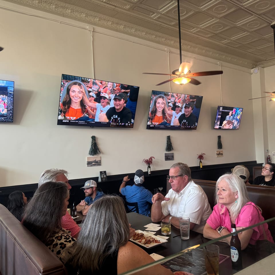 People dining in a casual restaurant with multiple TVs showing sports and ceiling fans.