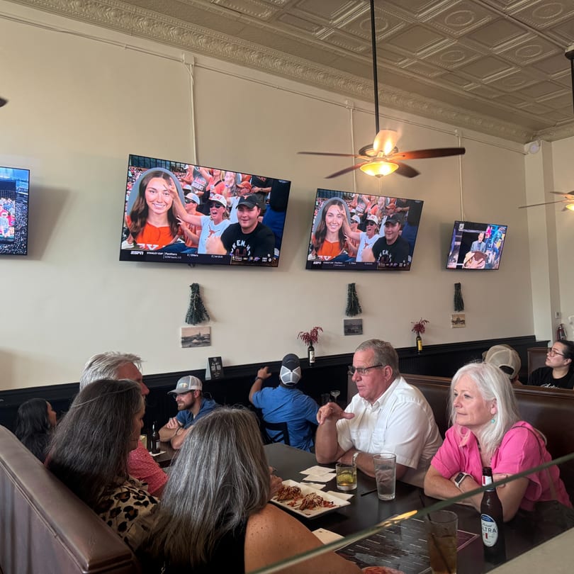 People dining in a casual restaurant with multiple TVs showing sports and ceiling fans.
