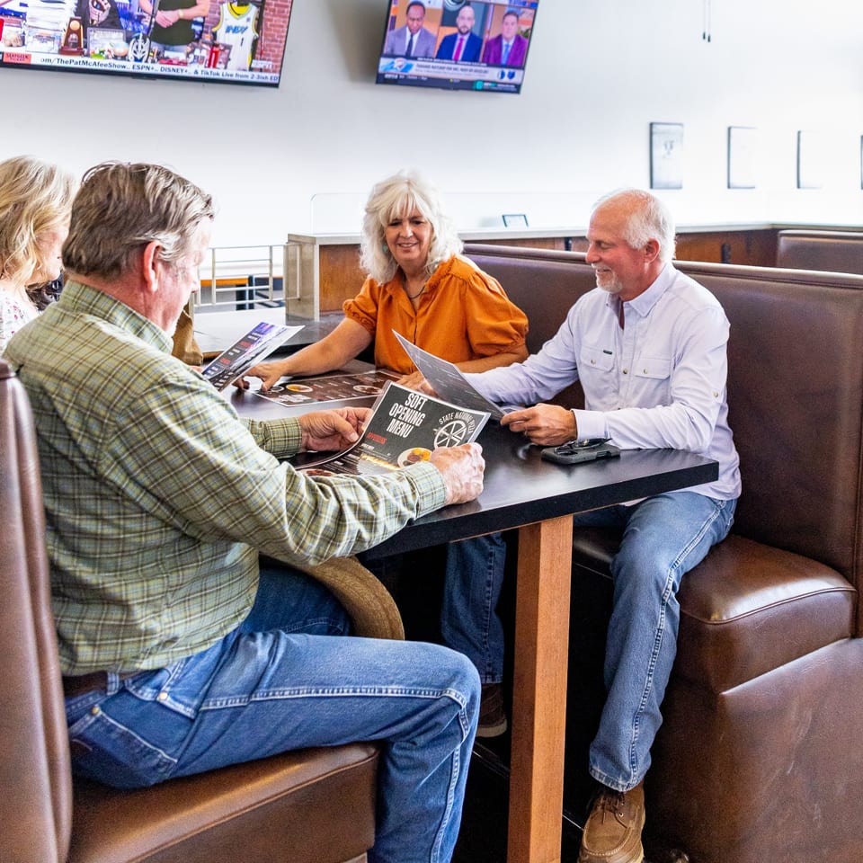 Four people in restaurant booths look at "Soft Opening Menu" and "State National Pizza" menus.