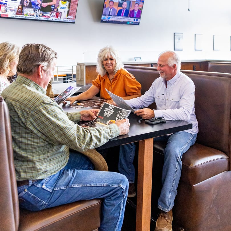 Four people in restaurant booths look at "Soft Opening Menu" and "State National Pizza" menus.