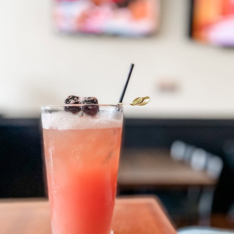 Pink cocktail with foam, garnished with two berries and a black straw on a wooden table.
