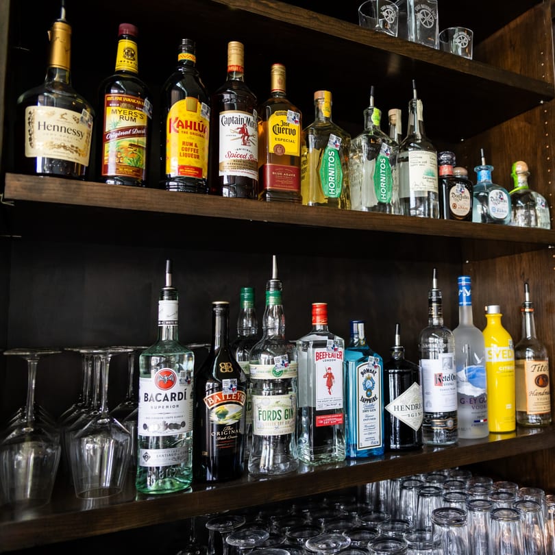 Two shelves filled with various liquor bottles and rows of clean bar glasses.