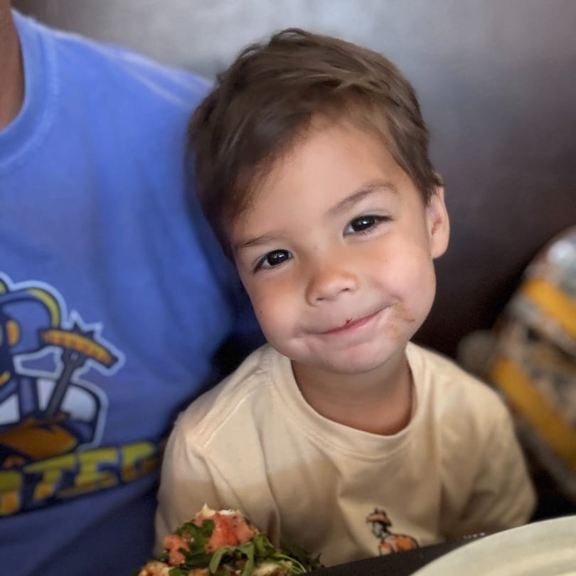 Happy child with a food smudge on their face, sitting at a restaurant table.