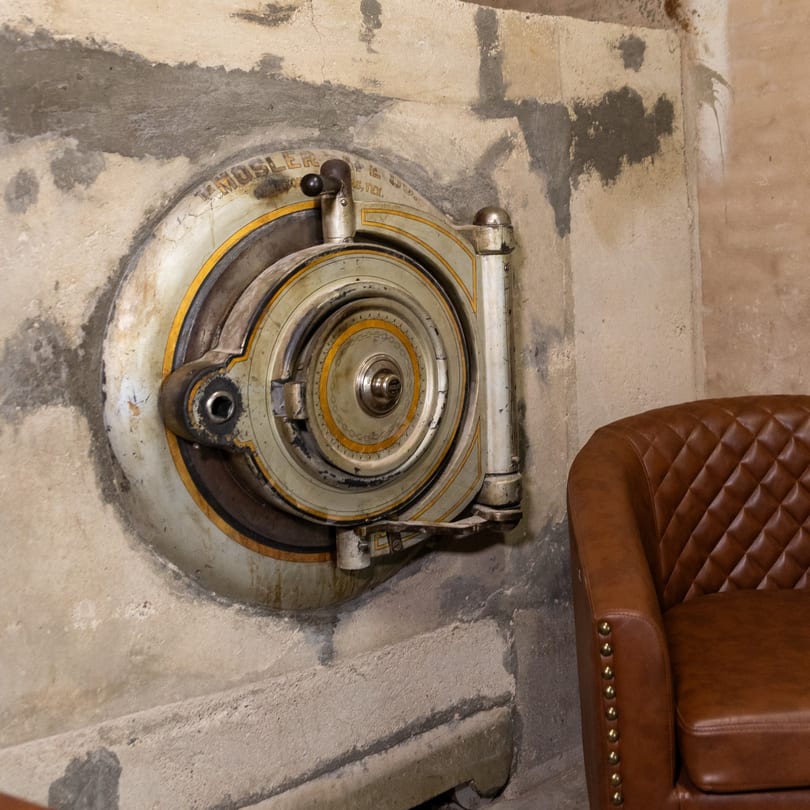 Vintage circular vault door embedded in a concrete wall next to a brown leather armchair.
