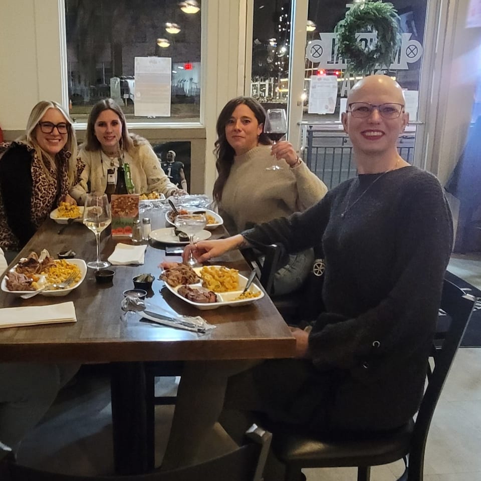 Four women smiling, dining on BBQ and mac and cheese at a restaurant table.