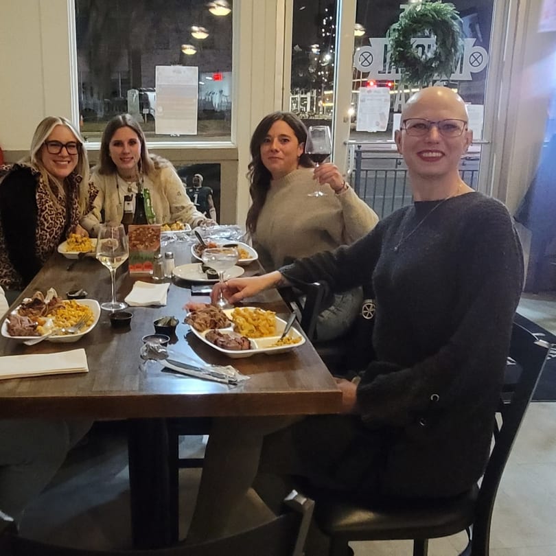 Four women smiling, dining on BBQ and mac and cheese at a restaurant table.