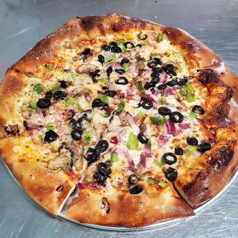 Freshly baked pizza topped with black olives, green peppers, red onions, and mushrooms.