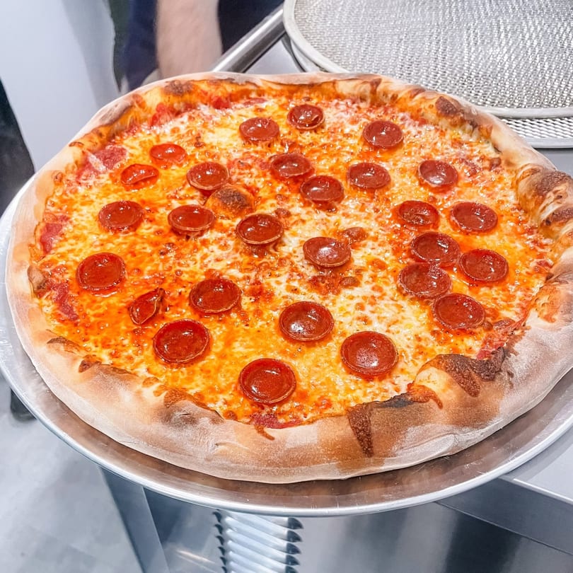 Whole pepperoni pizza with melted cheese and crispy crust on a metal tray.